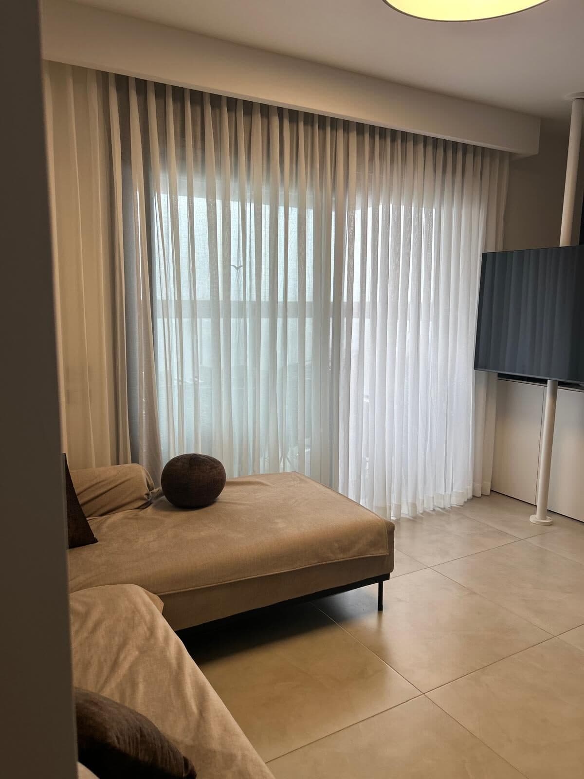 וילון מסך לבן על דלת מרפסת בסלון עם ספה בגוון קאמל